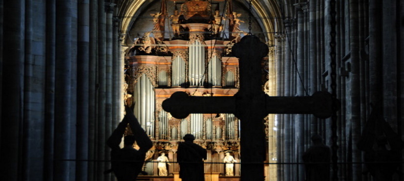 Blick in den Dom mit Licht an der Orgel und das dunkle Kreuz im Vordergrund.